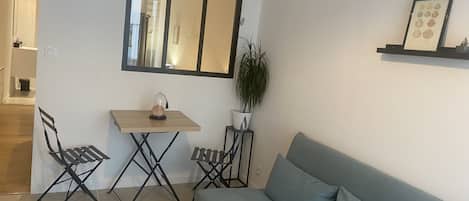 Een woonkamer met een bank, een kleine tafel, twee stoelen, een spiegel en een plant in pot.