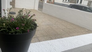 A balcony with a potted plant and a view of a street with buildings and a car. - Appartement T2 Avec Terrasse de 20m2 à Proximité des Plages (Étel)
