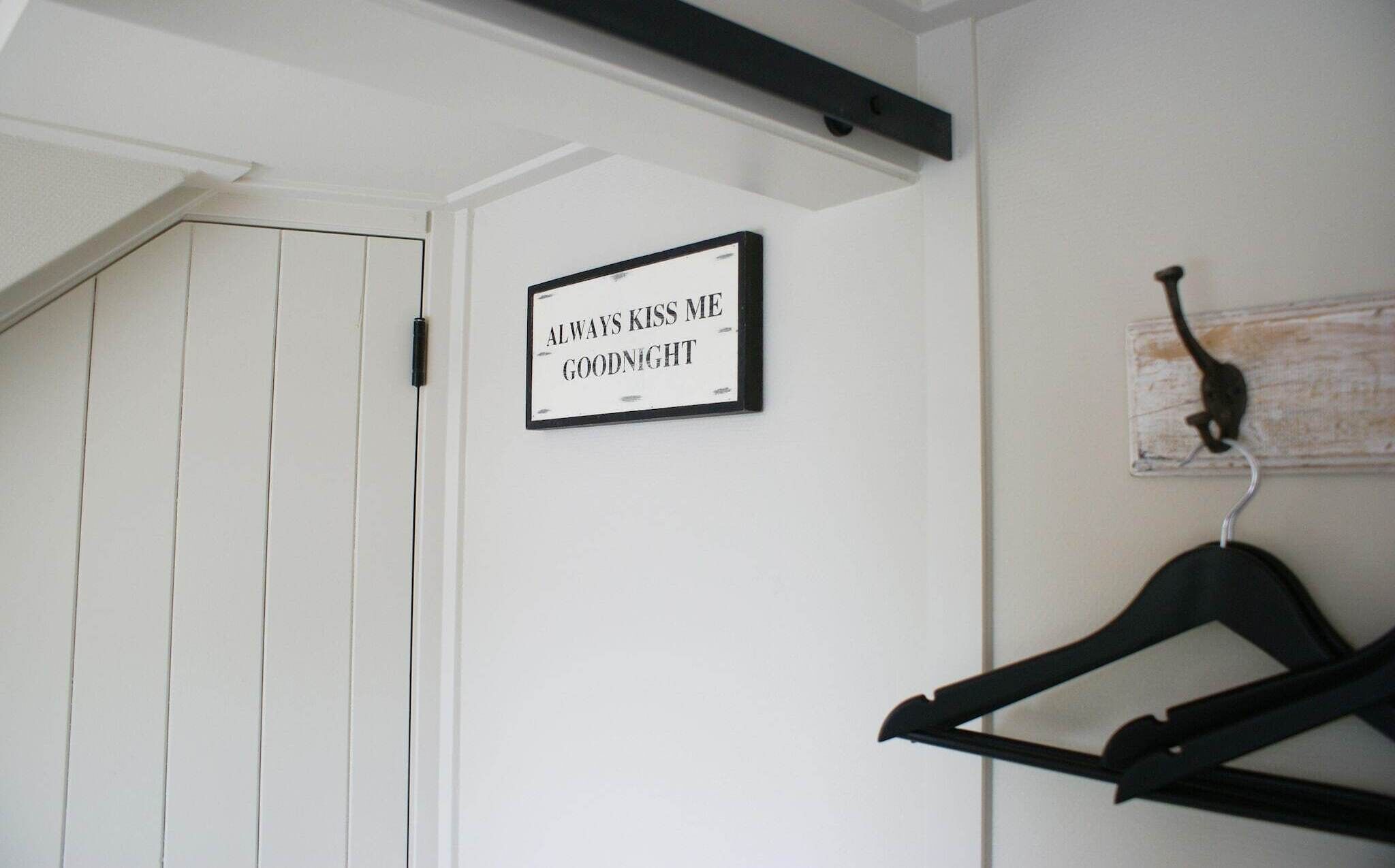 A white door with a sign that reads "ALWAYS KISS ME GOODNIGHT" and a black hanger on a wall.