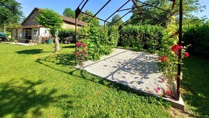 Un jardin agrémenté d’une pergola en métal, d’un chemin de gravier et d’une maison en arrière-plan.