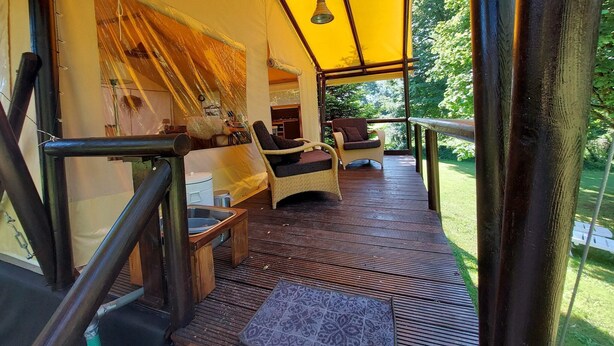Un espace extérieur abrité, aménagé avec des meubles en osier et une terrasse en bois.