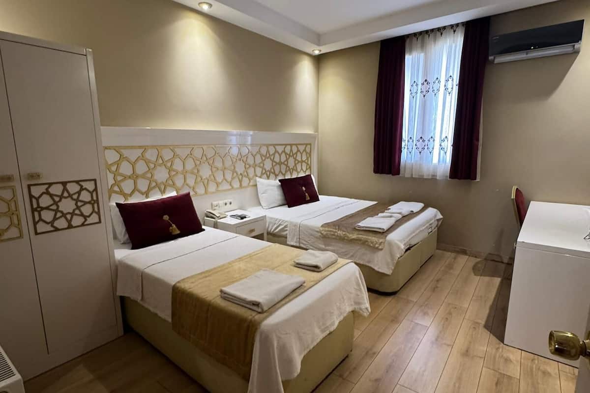 A hotel room with two beds, a wardrobe, a desk, and a window with curtains.