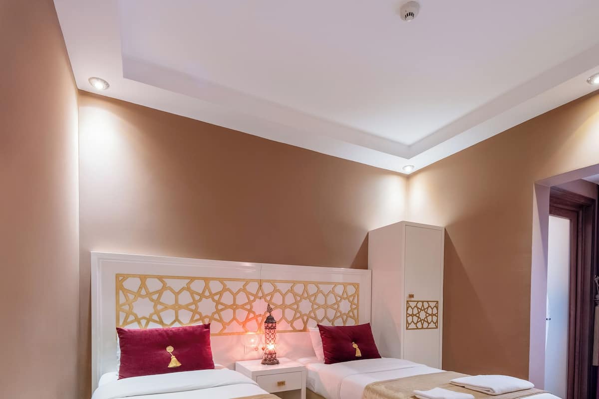 A double room with two beds, a white headboard with a geometric pattern, a small table with a lamp, and a radiator.