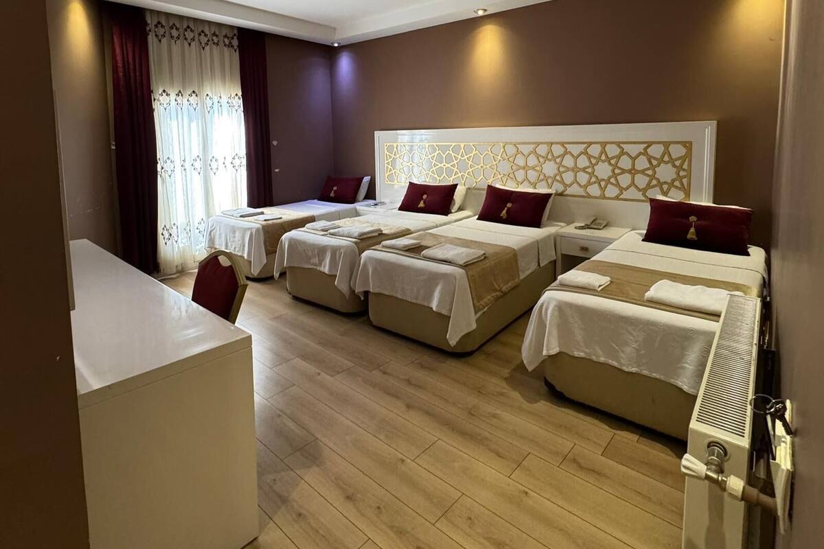 A hotel room with four single beds, a white desk, and a large window with curtains.