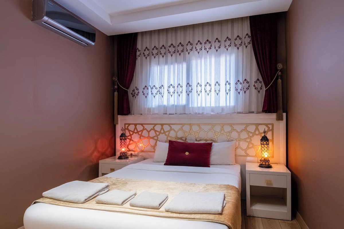 A modern bedroom with a large bed, bedside lamps, a window with curtains, and a ceiling light fixture.