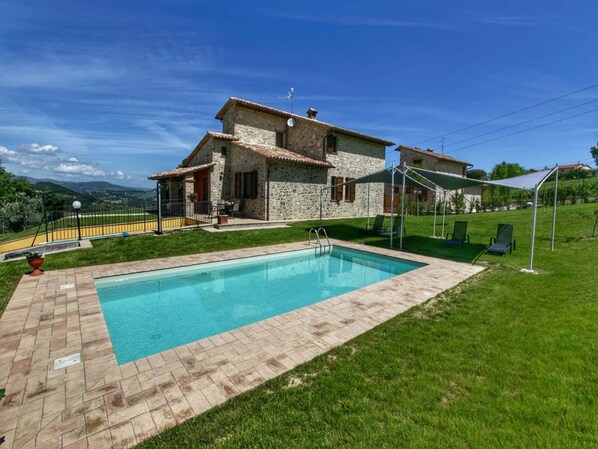 Ein Steinhaus mit Swimmingpool, einer überdachten Terrasse und Blick ins Grüne.