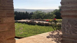 Un arc en pierre mène à un patio d’où l’on peut admirer des collines verdoyantes et un ciel dégagé.