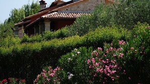 Un bâtiment en pierre, surmonté d’un toit en tuiles, entouré d’une végétation luxuriante et de plantes en fleurs.
