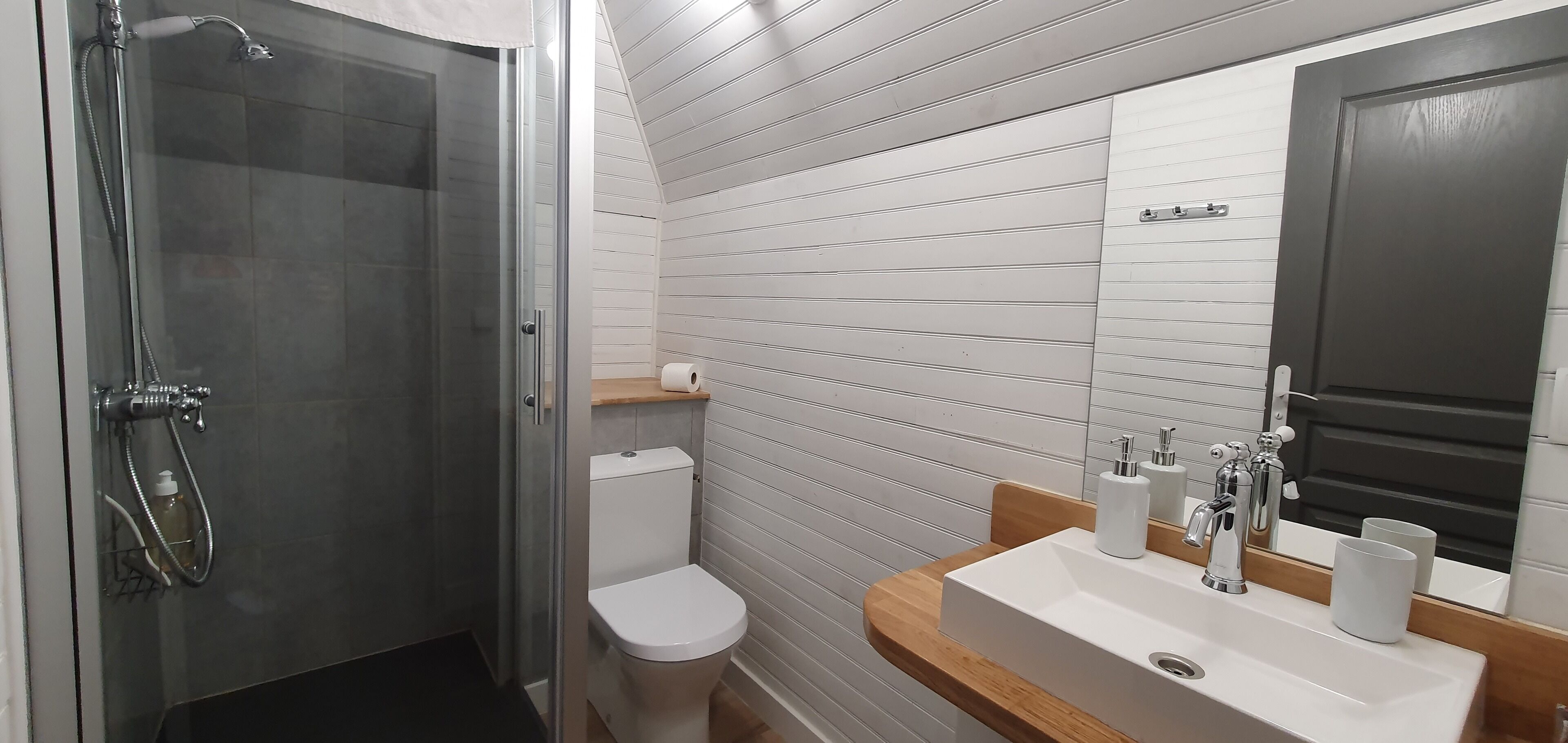 Ein modernes Badezimmer mit einer gläsernen Duschkabine, einer weißen Toilette und einem Holzwaschtisch mit Waschbecken und Spiegel.