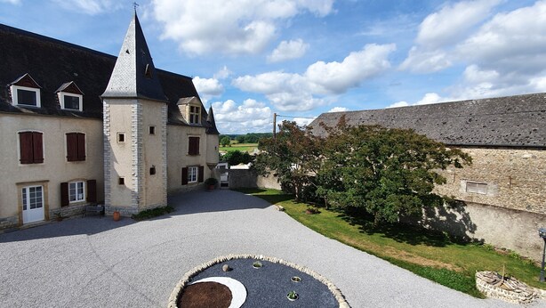 Un patio con una torre central, edificios de piedra y un área pavimentada con un jardín circular.