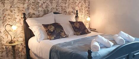 A bedroom with a bed, floral wallpaper, and a nightstand with a lamp.