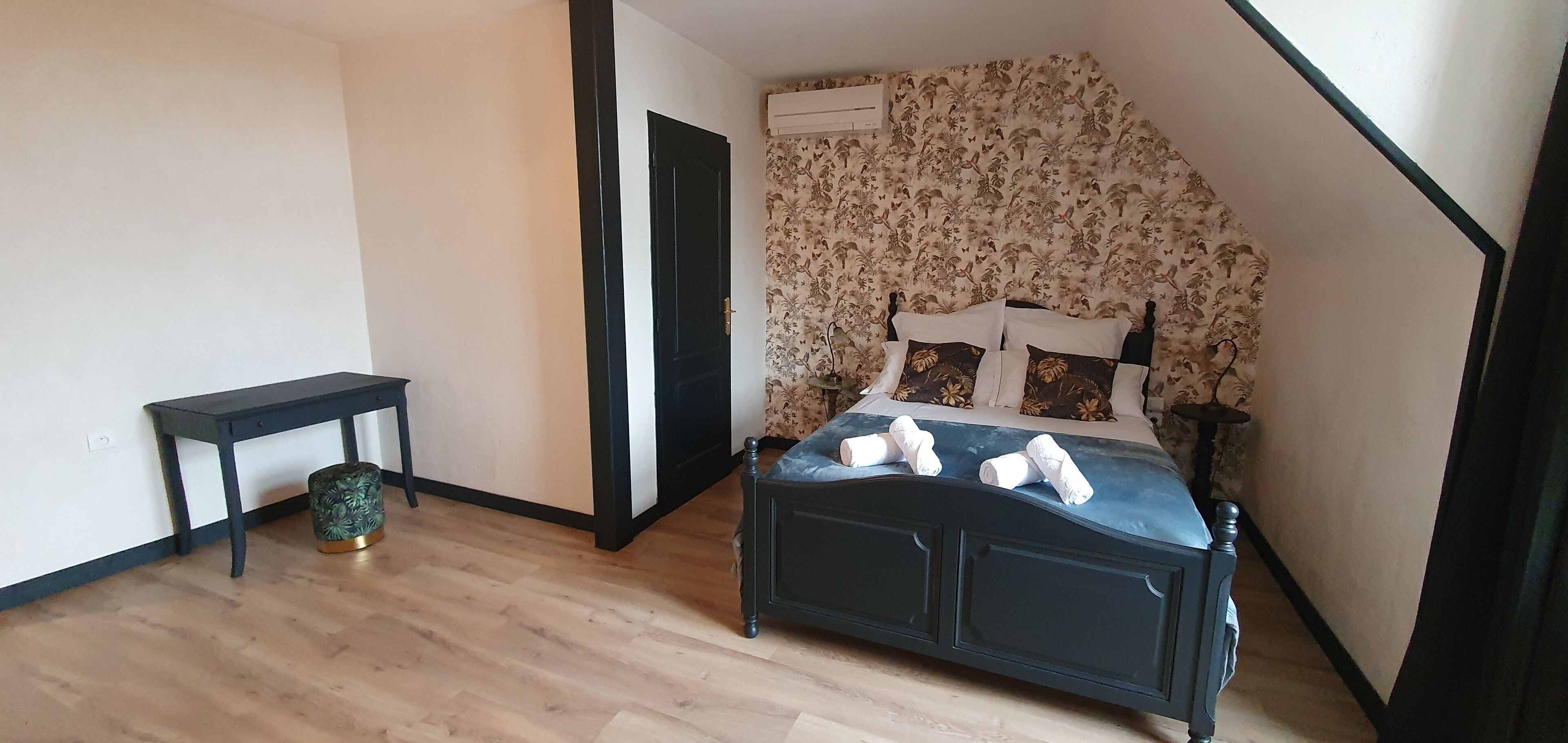 A bedroom with a bed, a small table, a chair, and a decorative wall.