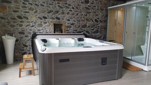 Un baño con pared de piedra, puerta de madera, cabina de ducha de vidrio y una bañera grande.
