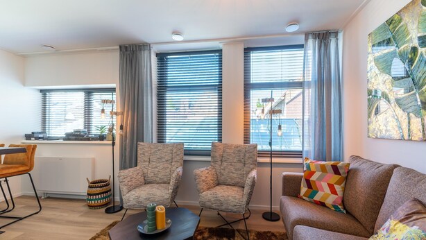 A modern living room with a sofa, two armchairs, a coffee table, and a dining area with a chair and table. - Modern renovated apartment in the heart of Sneek (Sneek)