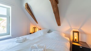 A bedroom with a large bed, two bedside tables with lamps, a window, and exposed wooden beams. - Modern renovated apartment in the heart of Sneek (Sneek)