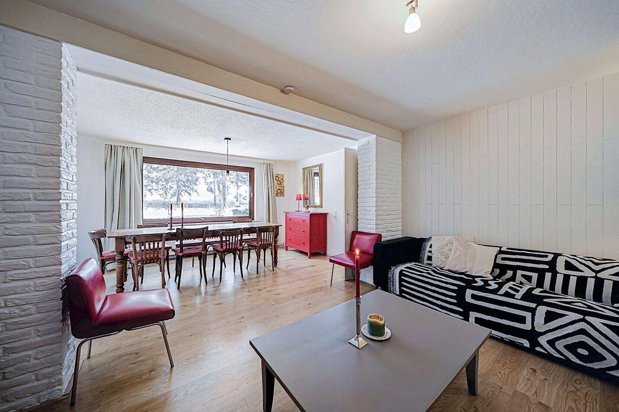 A living room with a sofa, a dining table with chairs, a red chair, and a lamp.