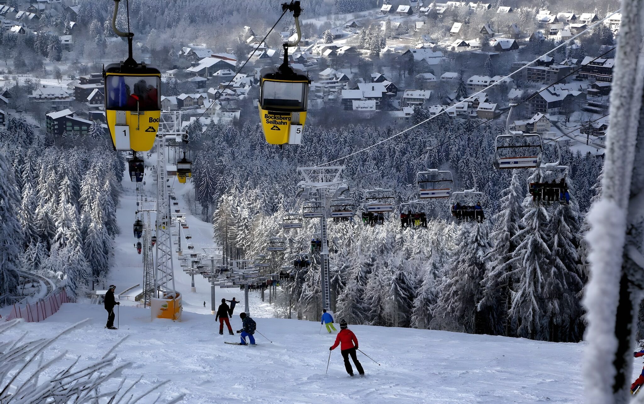 A ski lift with cabins, a snowy landscape, and a town in the background.