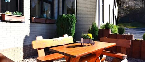 Ein Gartenmöbel-Set aus Holz mit Bank und Tisch vor einem Gebäude mit Fenstern und Blumentöpfen.