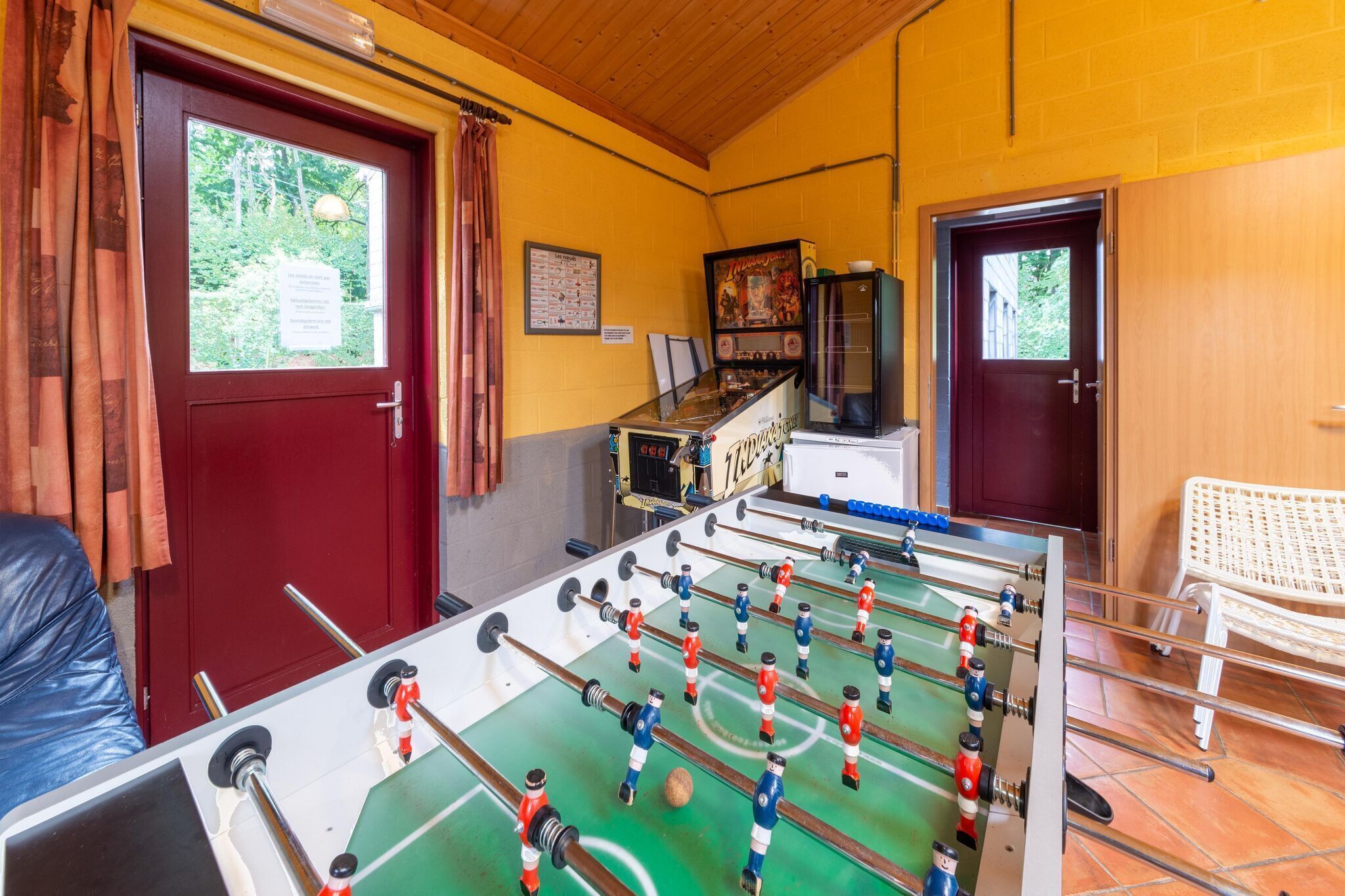Ett rum med ett fotbollsspel, en röd dörr och ett fönster med gardiner.