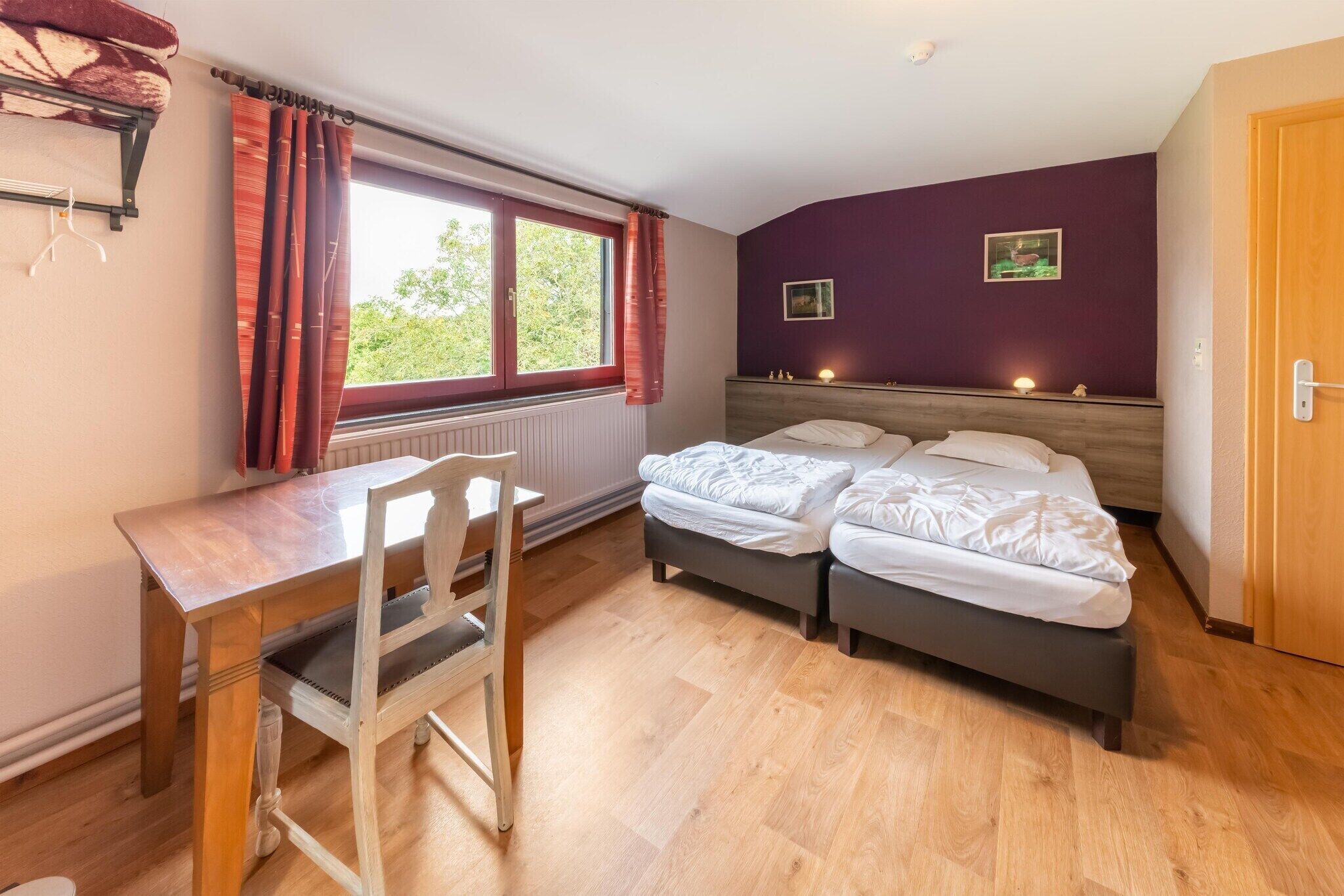A bedroom with two beds, a wooden desk, a chair, and a window with curtains.