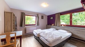 Ein Schlafzimmer mit zwei Betten, einem Holzstuhl, einem Heizkörper und einem Fenster mit Vorhängen.