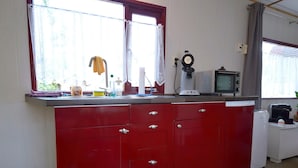 A kitchen with red cabinets, a window with curtains, a clock, and a microwave. - Apartment in Meisberg with In-house Catering (Meisburg)