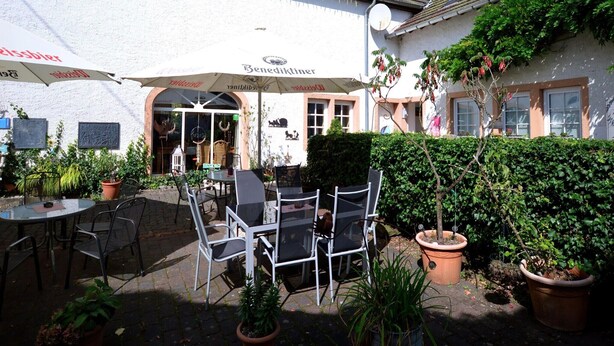 An outdoor seating area with tables and chairs, a white building with a sign, and potted plants. - Apartment in Meisberg with In-house Catering (Meisburg)