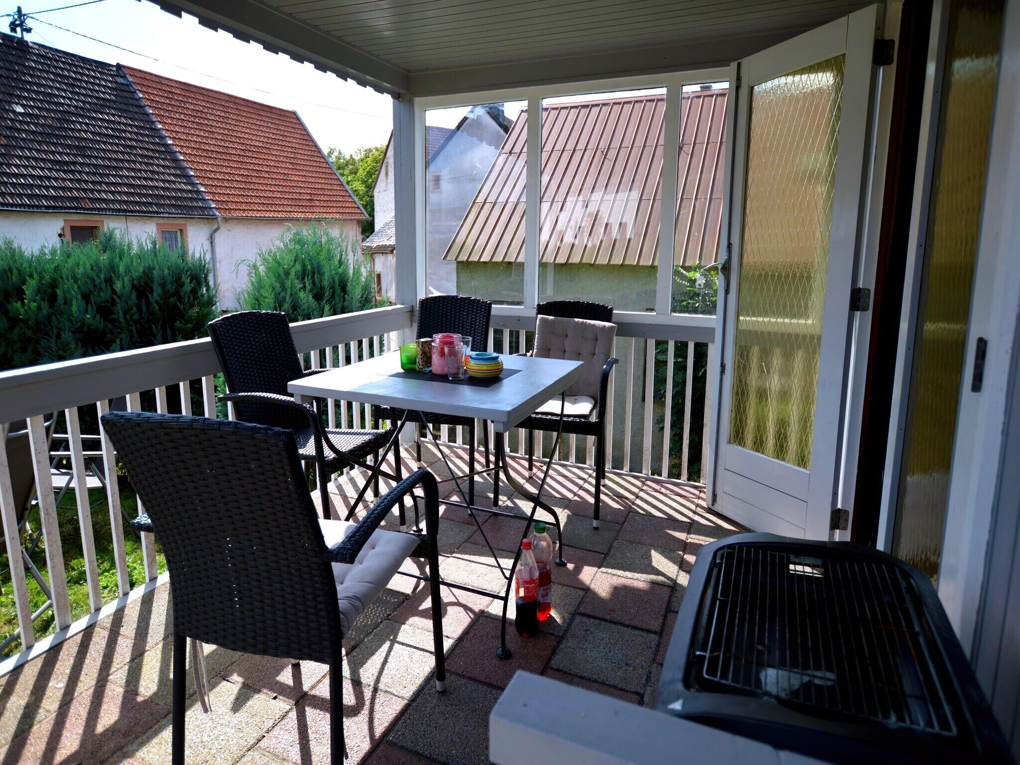 A covered patio with a table and chairs, a grill, and a view of neighboring houses.