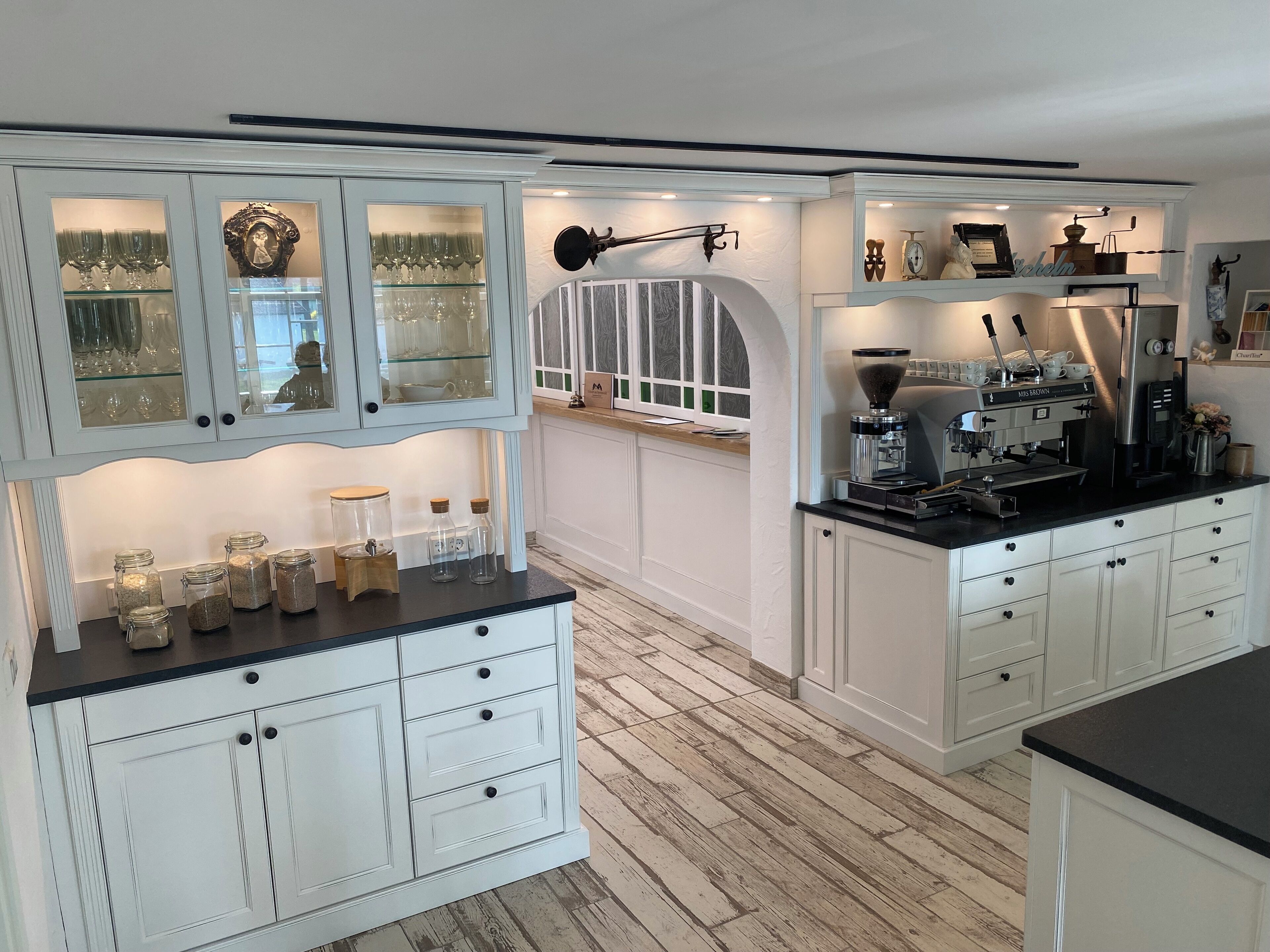 A kitchen with white cabinetry, a coffee machine, and glass-fronted cabinets displaying kitchenware.