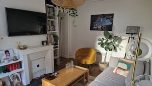 Ett vardagsrum med en tv, en bokhylla, en soffa, ett soffbord och en stor växt.