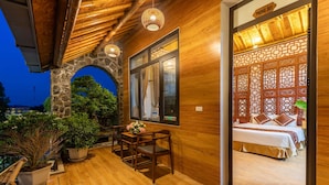 A wooden exterior with a stone archway, a balcony with a table and chairs, and a bed with a wooden headboard inside. - Tam Coc Serenity Hotel & Bungalow (Nam Hoa Lu)