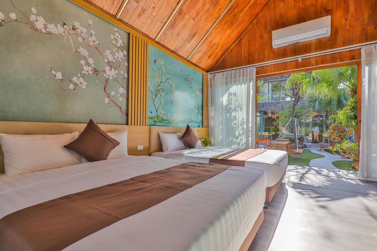 Une chambre d’hôtel avec deux lits, une grande fresque murale, un plafond en bois et une vue sur un jardin.