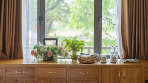 A wooden desk with a vase of flowers, a basket, and a window with curtains. - Tam Coc Serenity Hotel & Bungalow (Nam Hoa Lu)