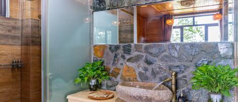Une salle de bain avec un mur en pierre, un lavabo avec un receveur en pierre et une douche.