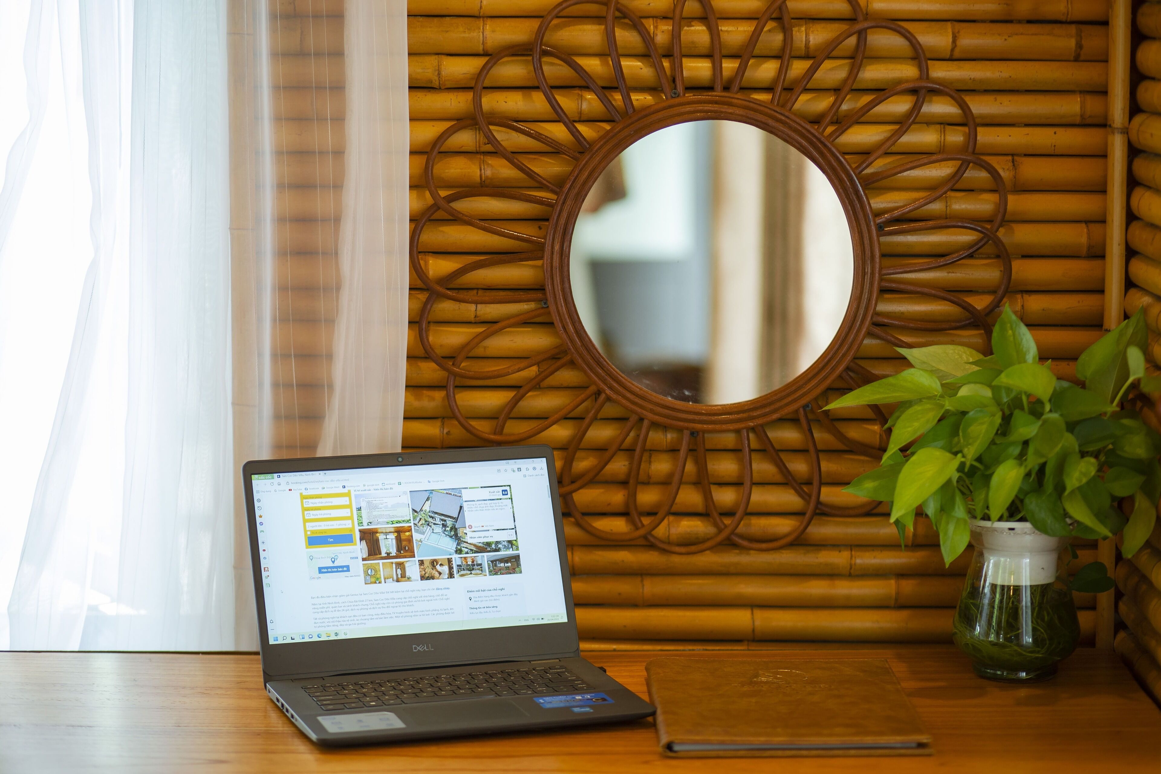 A laptop on a wooden table with a bamboo wall and a mirror.