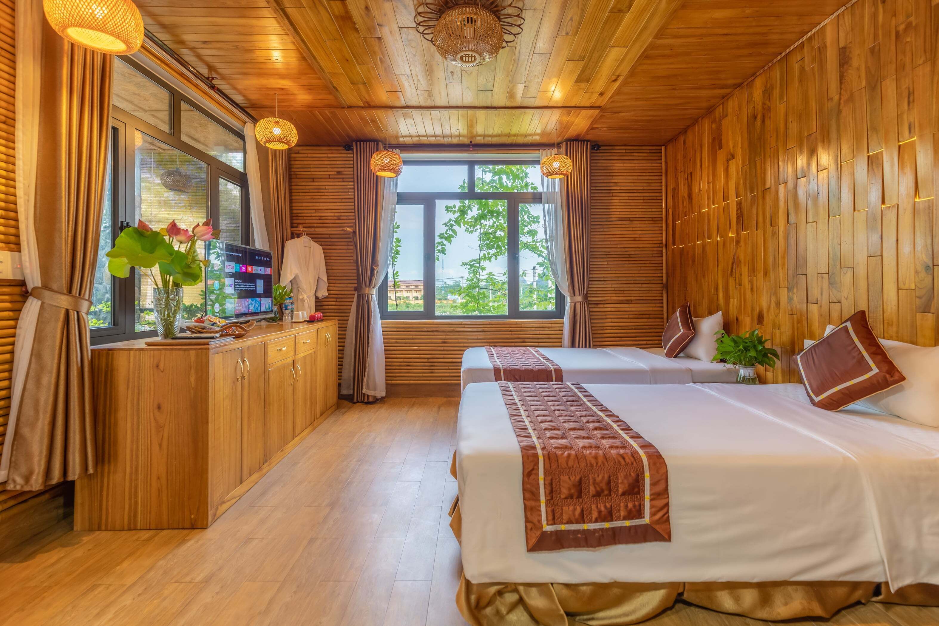 A wooden-paneled room with two beds, a wooden desk, and a large window with curtains.