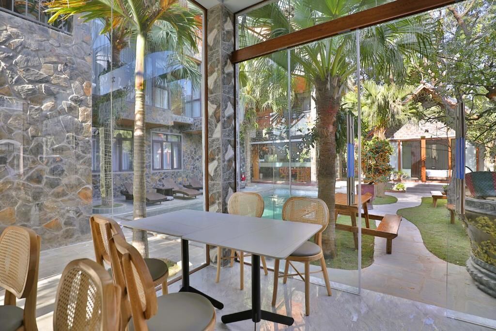 A glass-enclosed patio with a table and chairs, a pool, and a stone wall.