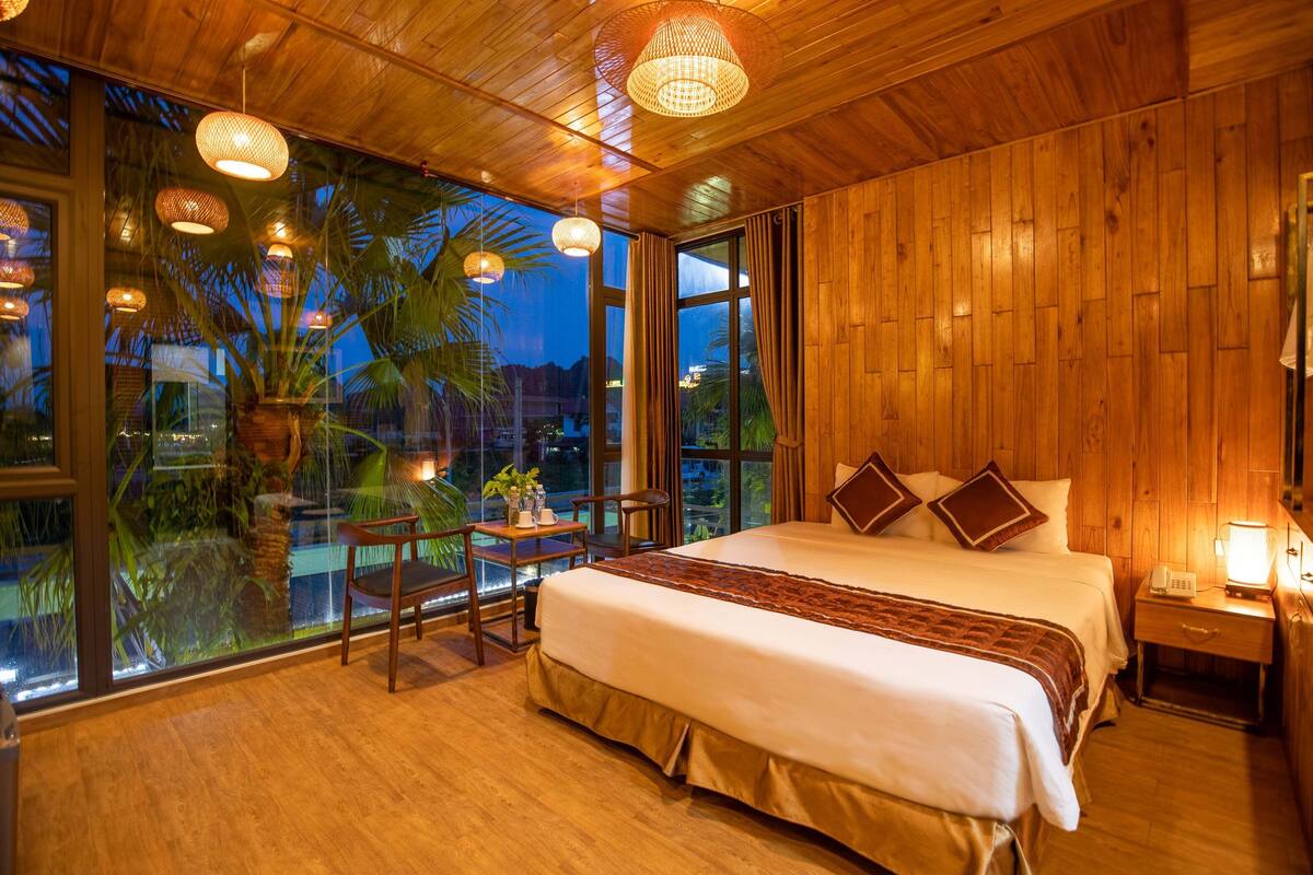 Une chambre spacieuse avec un grand lit, des murs en bois et une vue sur les palmiers, visible à travers de grandes fenêtres.