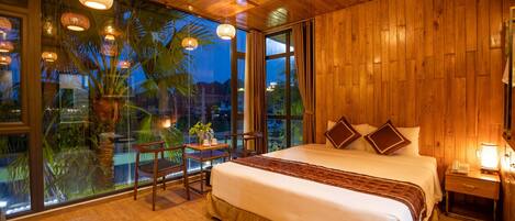 Un dormitorio amplio con una cama grande, paredes de madera y vistas a palmeras a través de ventanas grandes.