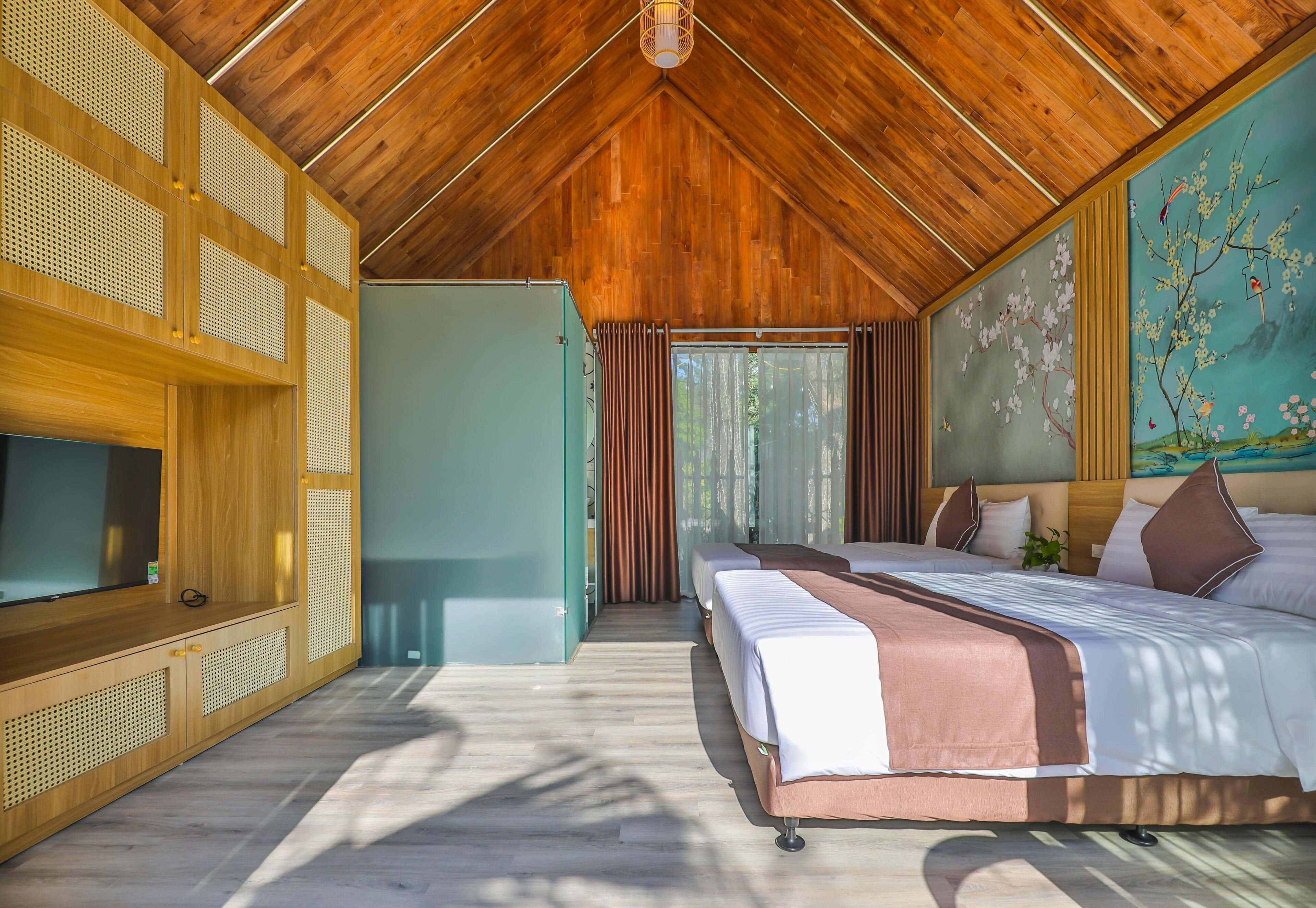 A bedroom with a wooden ceiling, a bed with white and brown bedding, a TV on the left, and a painting on the wall.