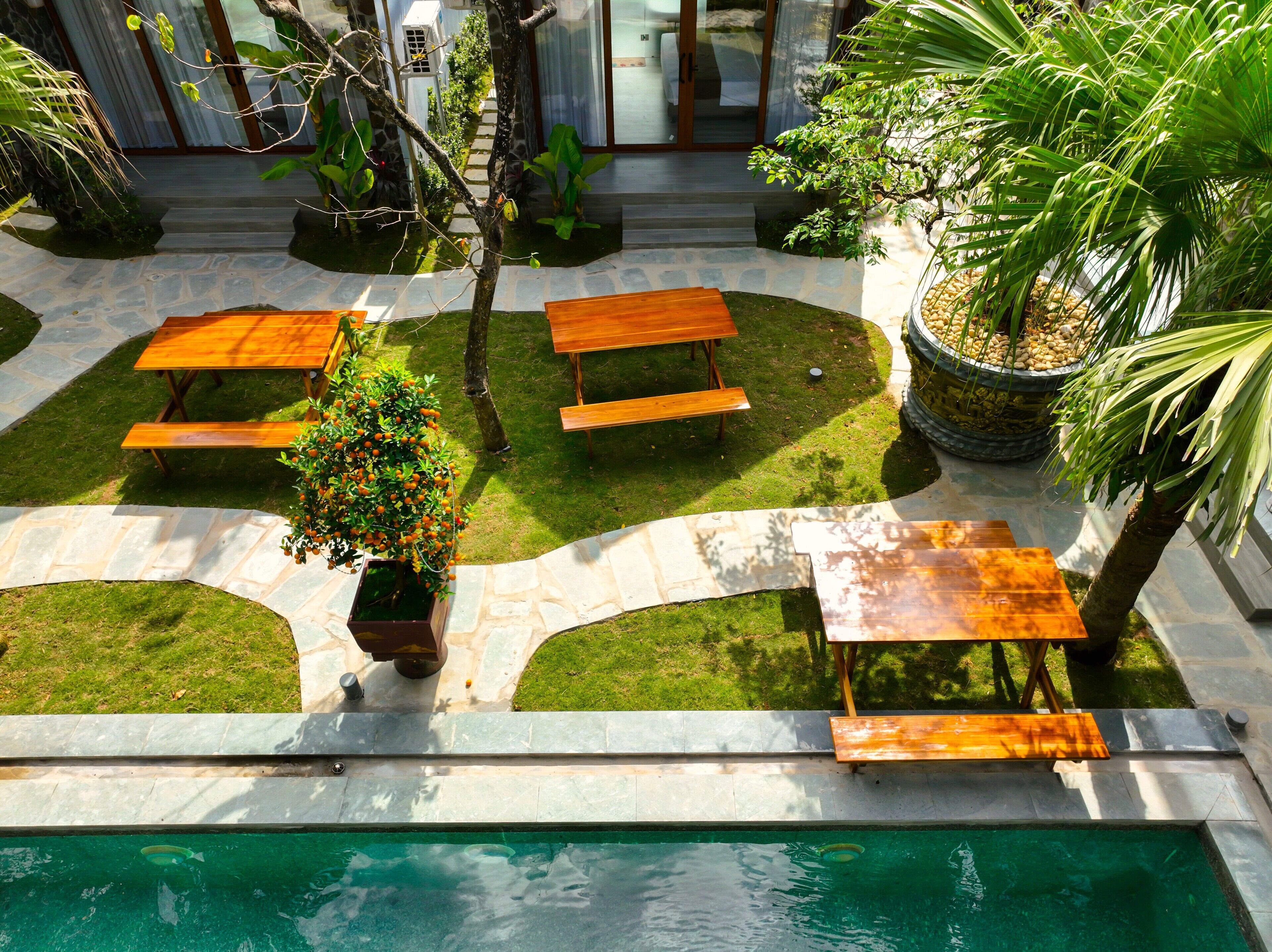 A poolside area with wooden benches, a small tree, and a stone pathway leading to a building.