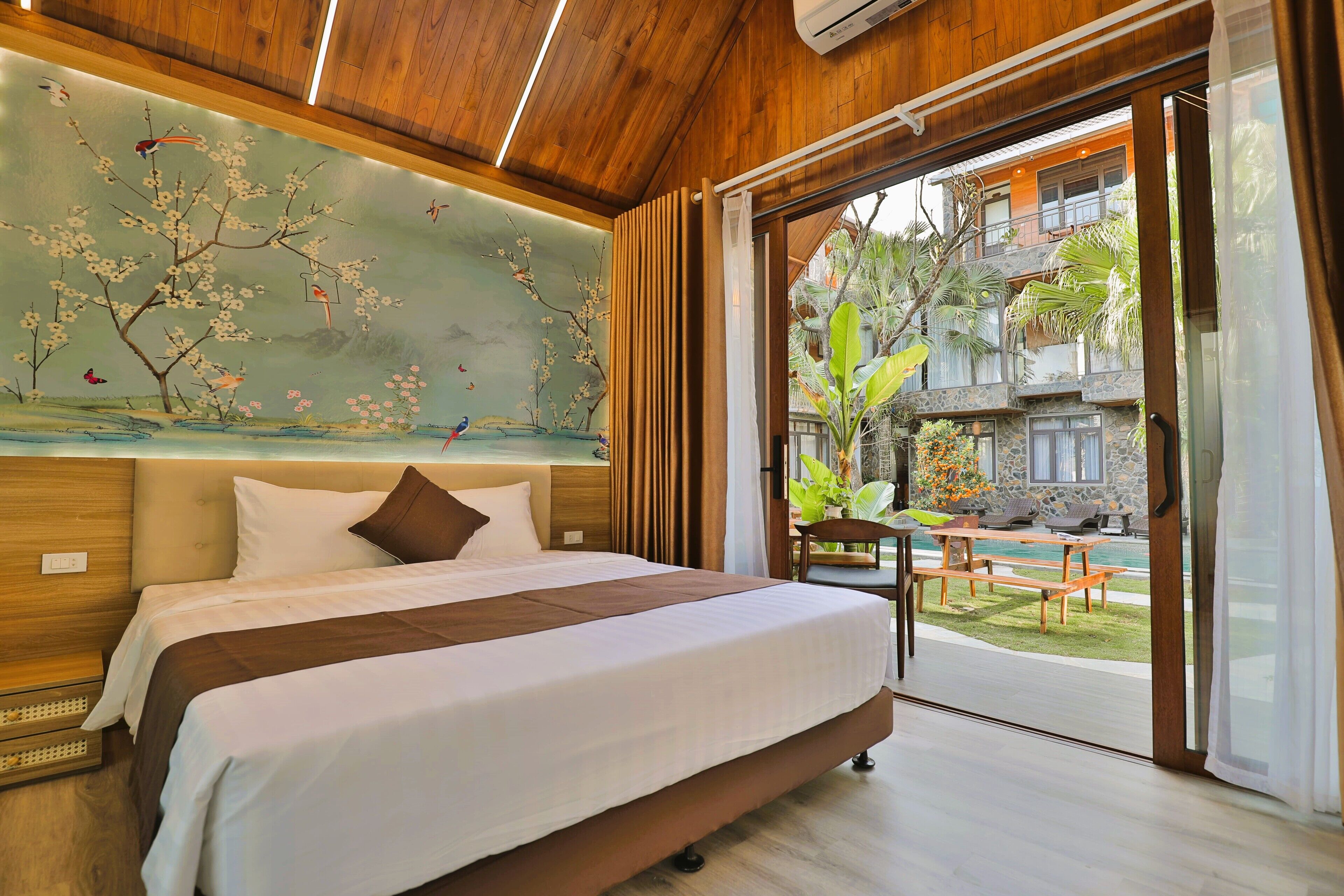 A spacious bedroom with a large bed, a mural on the wall, and a view of an outdoor pool area.