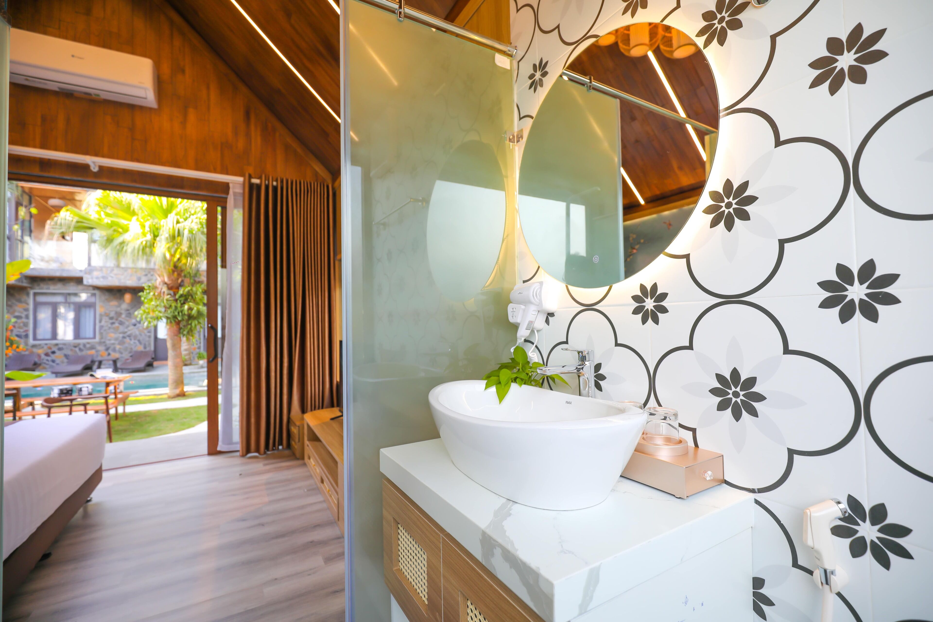 A modern bathroom with a large mirror, white sink, and a view of a pool and outdoor seating area.