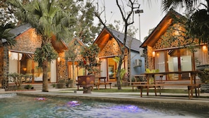 A resort with stone and wooden buildings, a swimming pool, and outdoor seating areas. - Tam Coc Serenity Hotel & Bungalow (Nam Hoa Lu)