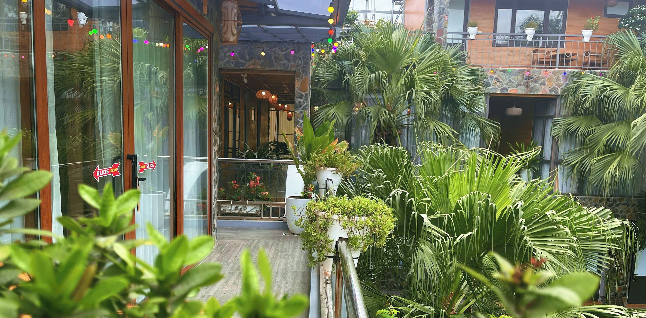L’entrée d’un hôtel avec une porte en verre, un panneau indiquant la présence d’un toboggan, et un balcon agrémenté de plantes en pot et d’un mur en pierre.