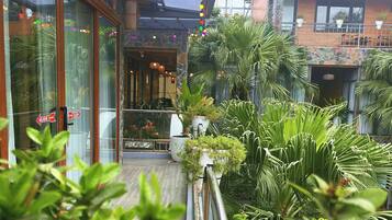 L’entrée d’un hôtel avec une porte en verre, un panneau indiquant la présence d’un toboggan, et un balcon agrémenté de plantes en pot et d’un mur en pierre.