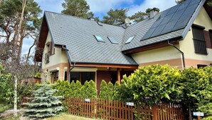 Una casa de dos pisos con techo inclinado, paneles solares y cerco de madera.