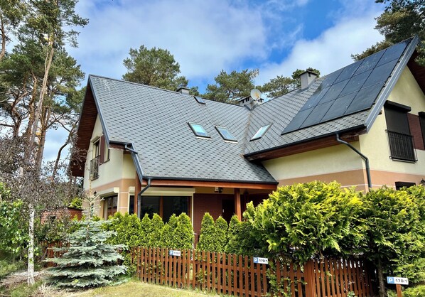 Een huis met twee verdiepingen, een schuin dak, zonnepanelen en een houten omheining.