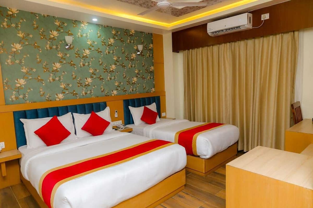 Quarto de hotel com duas camas, cada uma com roupa de cama vermelha e branca, papel de parede floral e um ventilador de teto.