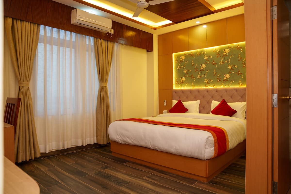 Quarto de hotel com uma cama grande, piso de madeira, ventoinha no teto e painel decorativo na parede.